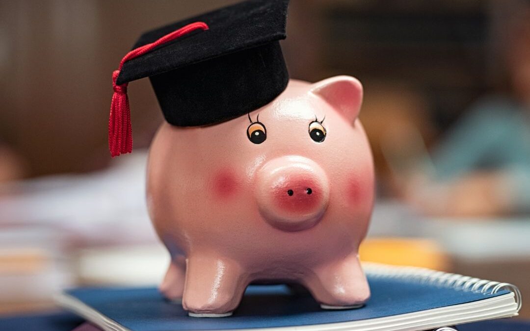 A toy pig wearing a graduation cap sits atop a stack of notebooks