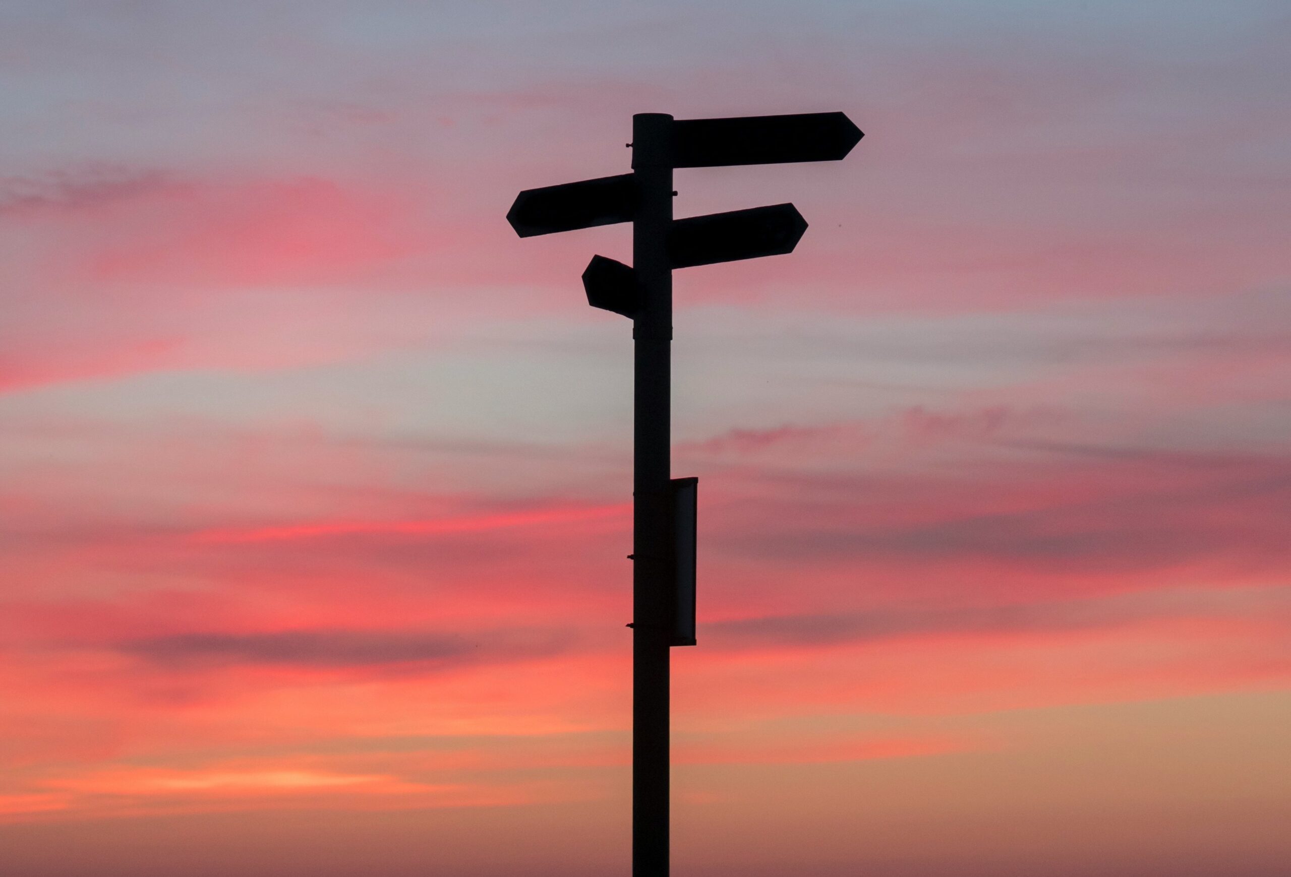 A signpost at dusk pointing the direction to places in the distance